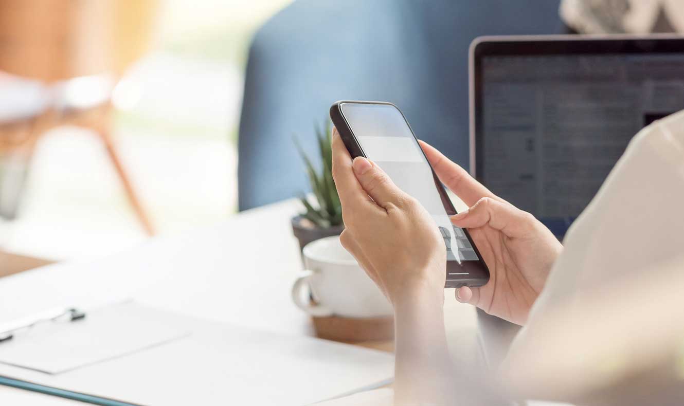 Business woman holding cell phone at a desk.